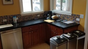 A kitchen with a dishwasher, trash bins, a coffee maker, and a window with a view of the street. - Beautiful House with Panoramic SF Bay Views (San Francisco)