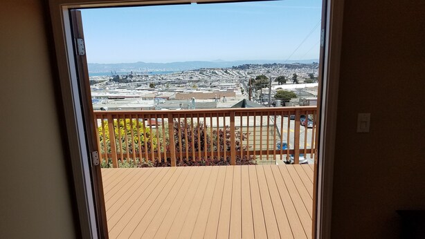 A view from a balcony with a wooden deck, overlooking a cityscape with buildings and a distant mountain range. - Beautiful House with Panoramic SF Bay Views (San Francisco)