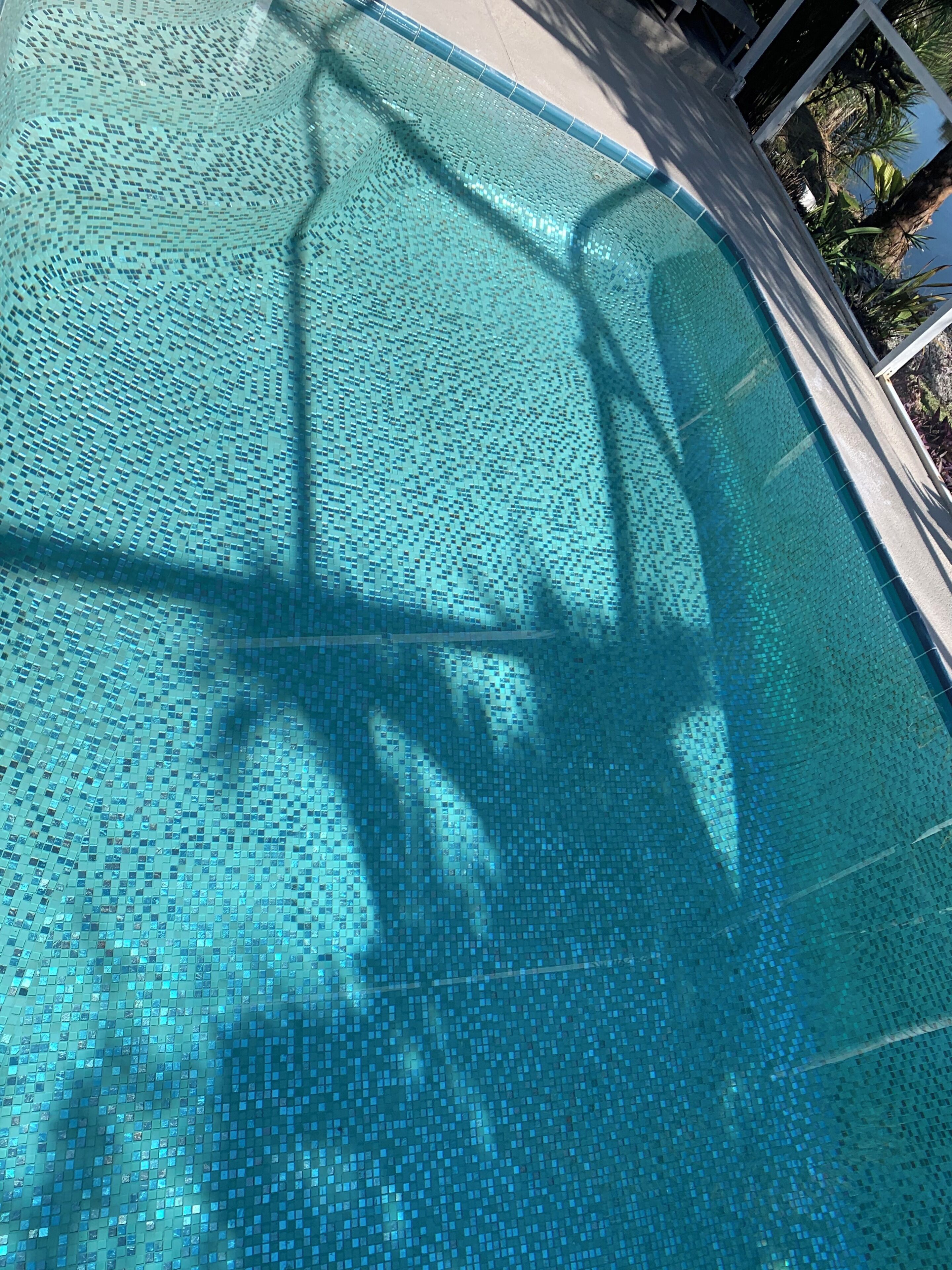 Vista clara de una piscina con superficie de azulejos y la sombra proyectada por una estructura.