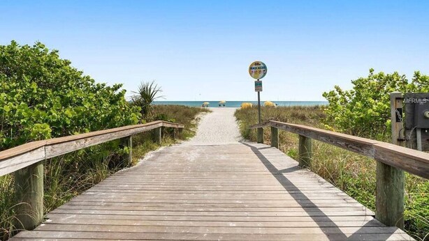 Pasarela de madera que conduce a una playa, con un cartel que indica que no se permite el baño.