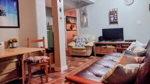 Una sala de estar con un sofá, un televisor, una mesa de comedor con sillas y una cocina al fondo.