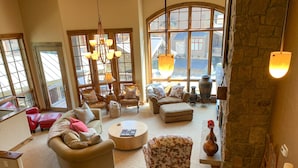 A spacious living room with a high ceiling, large windows, and a cozy fireplace.