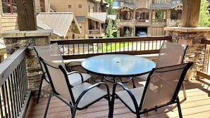 A wooden deck with a round table and four chairs, overlooking a large lodge with multiple buildings and a mountain backdrop.