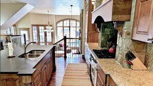 A spacious kitchen with a large island, stone fireplace, and a view of the backyard through large windows.