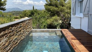 Una piscina con paredes de piedra y cubierta de madera, rodeada de árboles y vistas a la montaña.