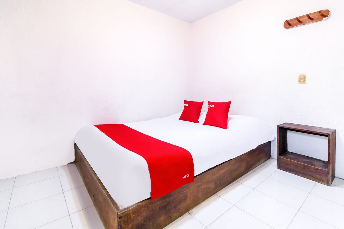 A bed with a wooden frame, white bedding, and red accents.