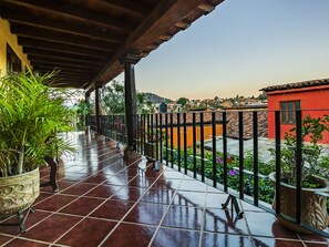 A covered outdoor area with tiled flooring, potted plants, and a view of a red building and surrounding neighborhood. - OYO Posada De Los Angeles, Pátzcuaro (Patzcuaro)