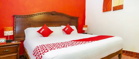 A hotel room with a wooden bed, red pillows, a white bedspread, and a red and white patterned throw.