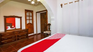 Une chambre avec une commode en bois, une chaise, un lit recouvert d’une couverture rouge et blanche, et un grand miroir.