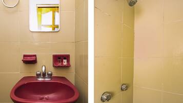 Un baño con un lavabo rojo, un espejo, un toallero y una ducha con pomo azul.