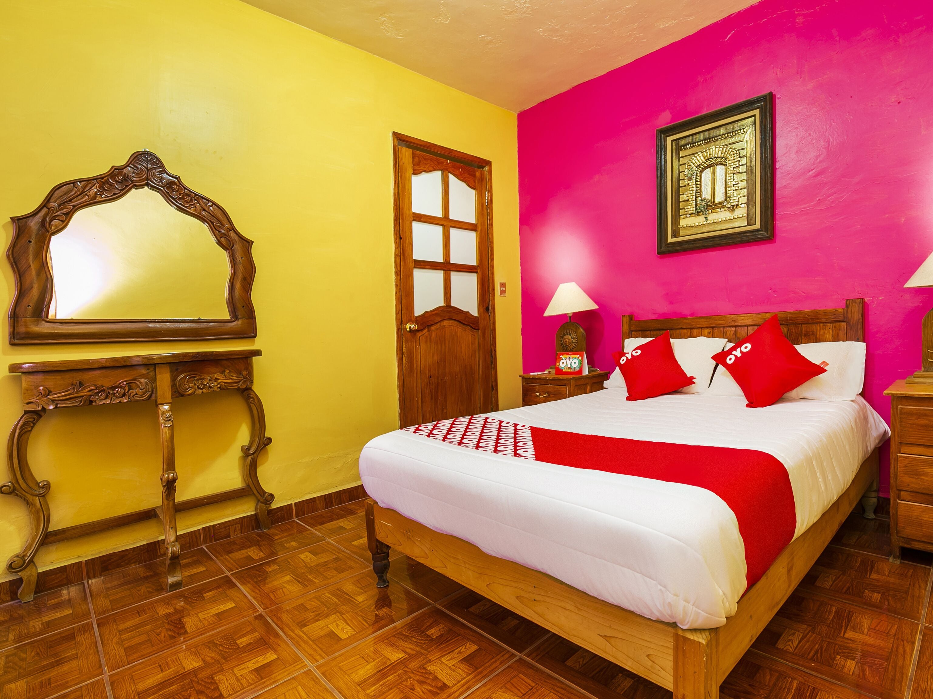 A bedroom with a wooden bed, a mirror, a door, and a wall with a framed picture.