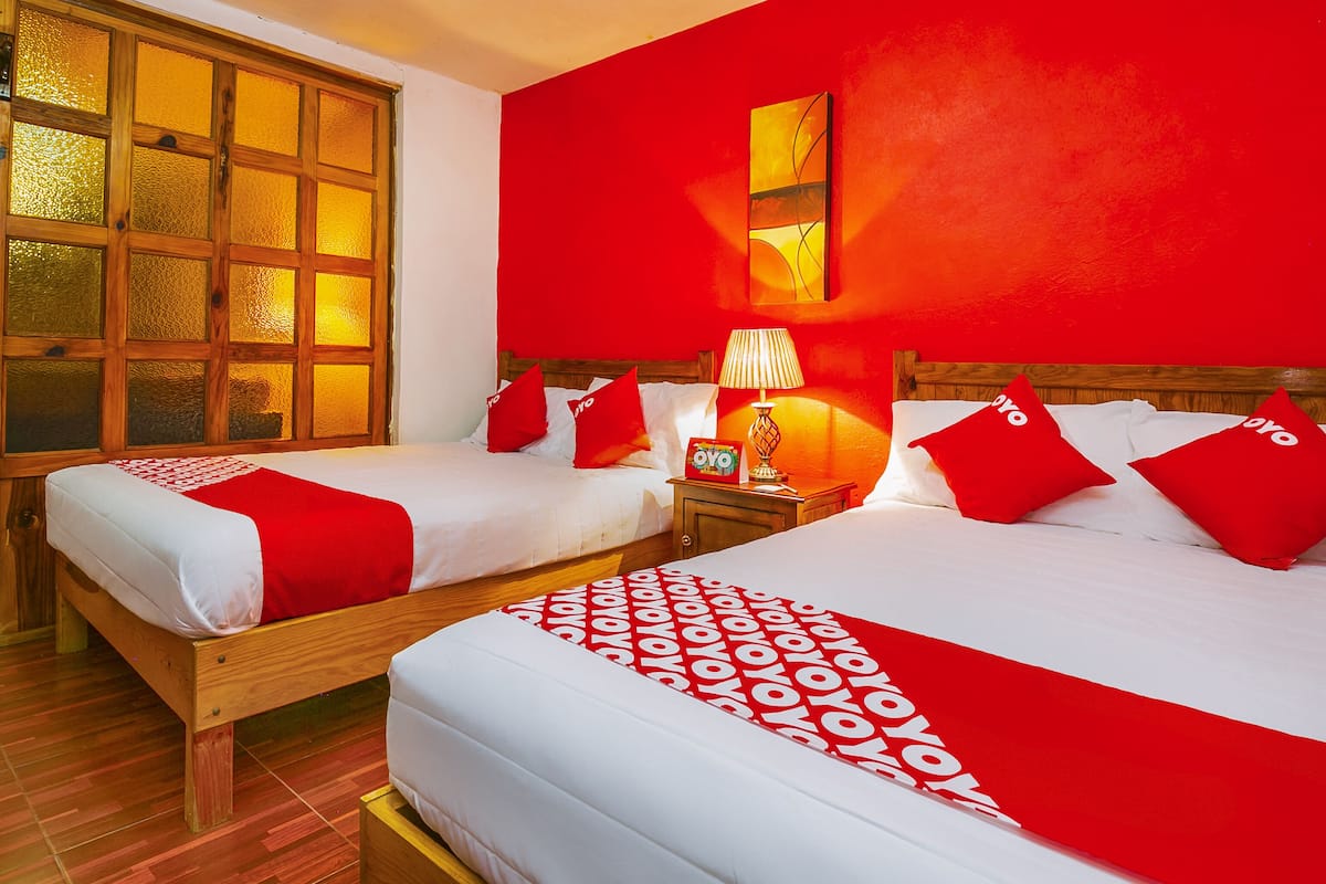 Ein Hotelzimmer mit zwei Betten, roten Akzenten, einem hölzernen Kopfteil und einem Fenster mit gesätzen Scheiben.