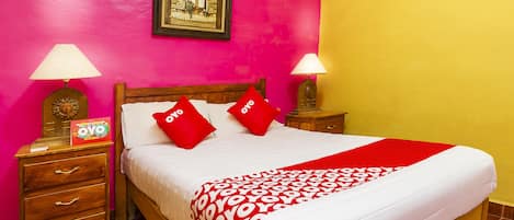 A bed with a red and white patterned bedspread, two red pillows, wooden nightstands with lamps, a framed picture on the wall, and a wooden headboard.