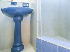 Un baño con un lavamanos pedestal azul, paredes de azulejos blancos y una zona de ducha con azulejos azules.