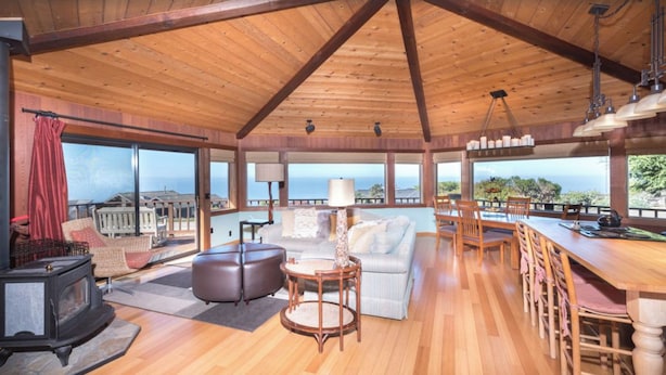 A spacious living area with a wooden ceiling, a fireplace, a sofa, a dining table with chairs, and large windows offering a view of the ocean. - September and October dates are available!!! Are Panoramic Ocean Views for you ? (Manchester)