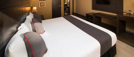 A hotel room with a large bed, a desk, a TV, and a mirror.