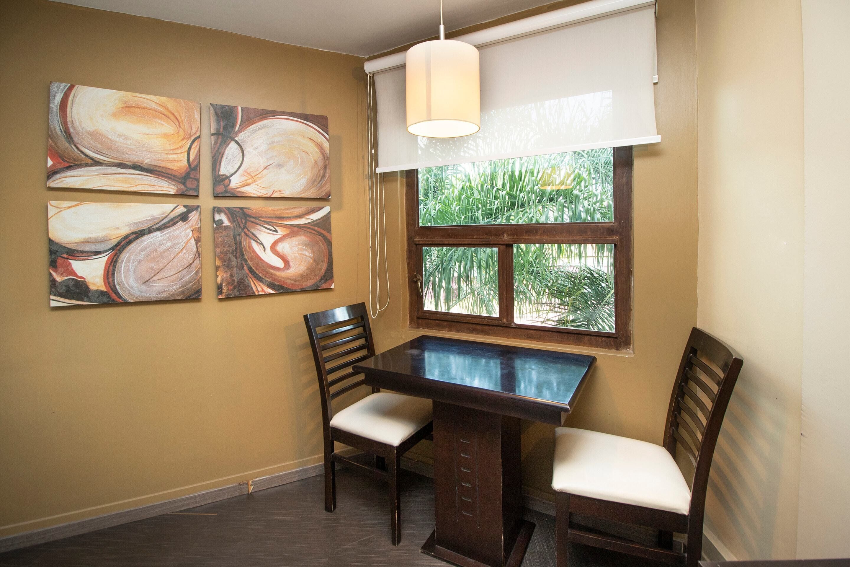A dining area with a table and chairs, a window with a view of greenery, and abstract wall art.
