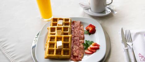 Un plato de desayuno con un gofre, tocino, fresas y un vaso de jugo de naranja.