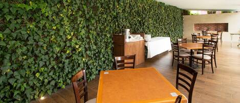 A restaurant with a green ivy wall, wooden tables, and chairs.
