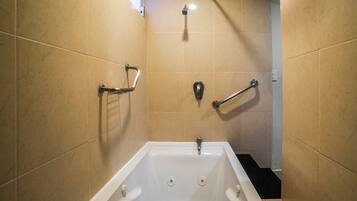 A bathroom with a white bathtub, grab bars, and a showerhead.