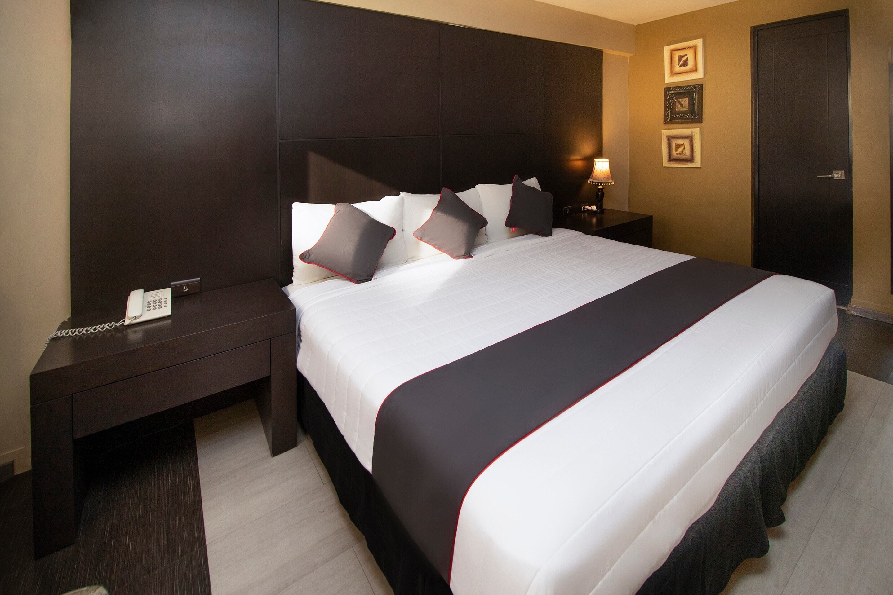 A hotel room with a large bed, dark wood headboard, bedside tables, and a phone on the left side.