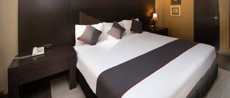 A hotel room with a large bed, dark wood headboard, bedside tables, and a phone on the left side.