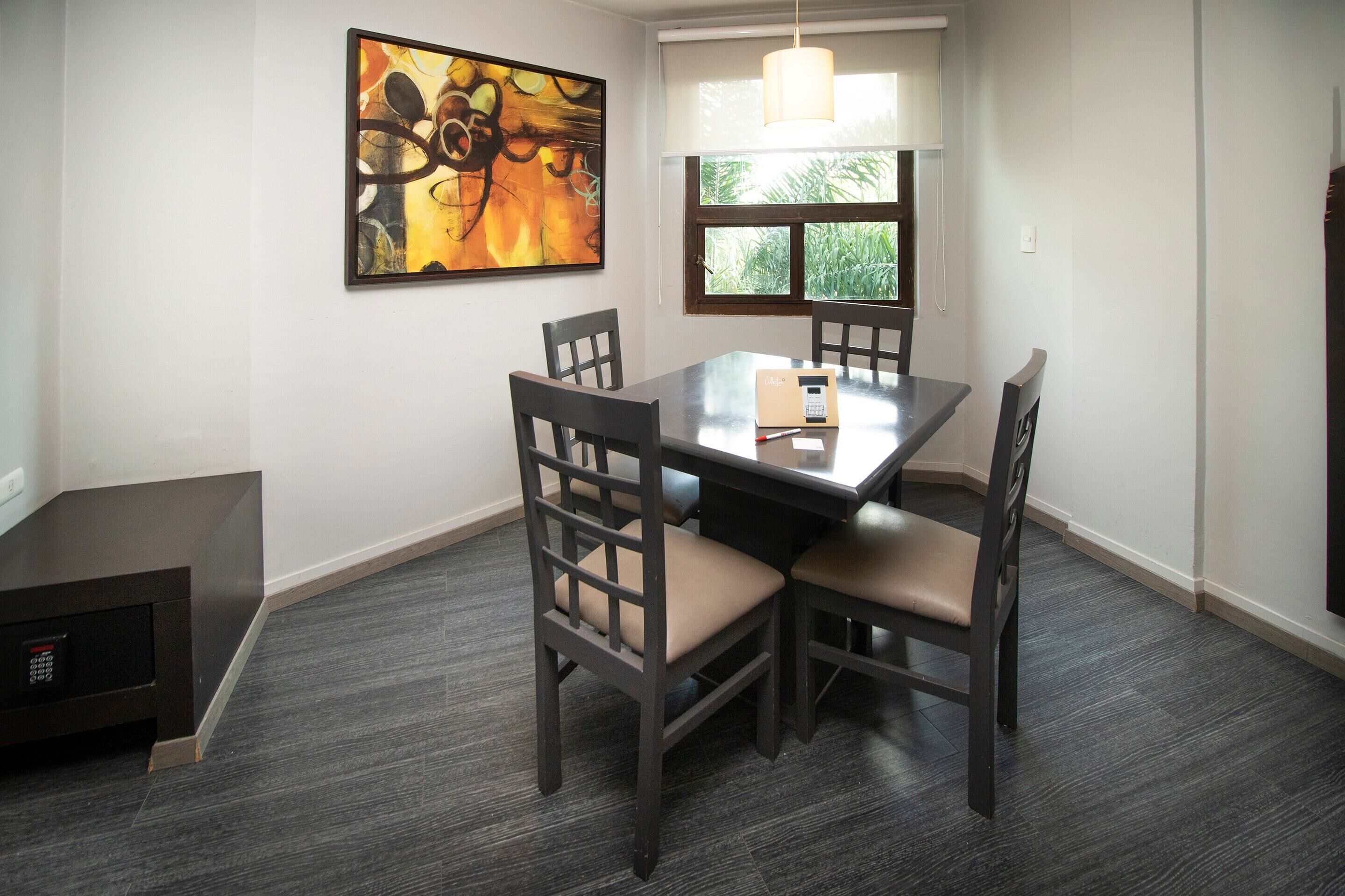 A dining area with a rectangular table, four chairs, and a painting on the wall.