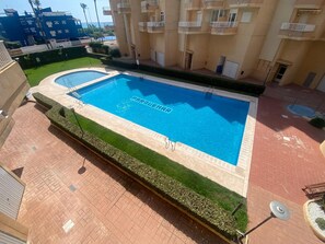 Ein rechteckiger Swimmingpool mit der Aufschrift 'PARQUE', umgeben von einer Pflasterterrasse und grünen Hecken.