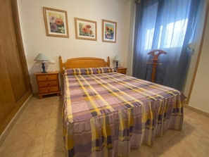 A bedroom with a wooden bed, two bedside tables with lamps, a wooden wardrobe, and three framed floral paintings on the wall.