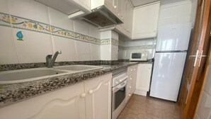 Eine Küche mit weißen Schränken, einer Granitabdeckung, einer Spüle, einem Herd, einer Mikrowelle und einem Kühlschrank.