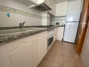 A kitchen with white cabinets, a granite countertop, a sink, a stove, a microwave, and a refrigerator.