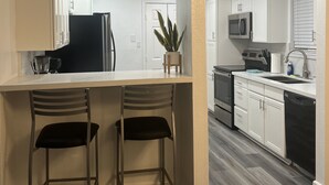 A modern kitchen with white cabinets, a central island with two bar stools, a refrigerator, microwave, and a dishwasher.