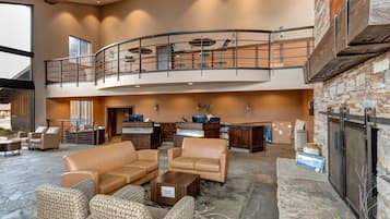 A spacious lobby with leather sofas, a fireplace, a reception desk, and a mezzanine with a balcony.