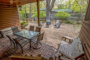 A covered patio with a glass table and chairs, surrounded by a brick patio and wooden deck.