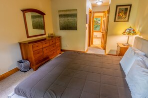 A bedroom with a large bed, wooden dresser, and a small table with a lamp.