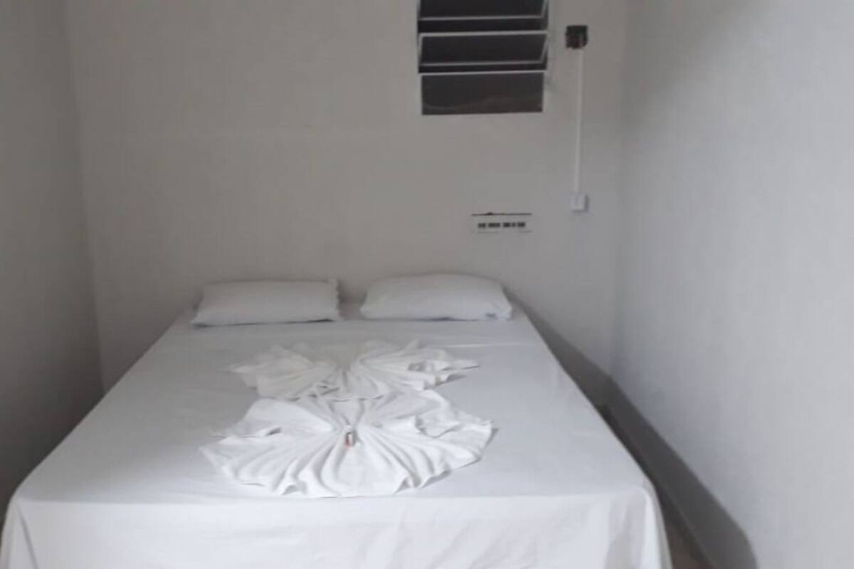 Ein schmales Zimmer mit einem Einzelbett, weißen Bettwäsche und schlichtem, klaren Design.