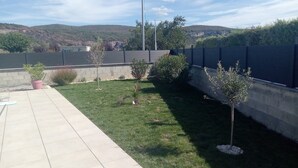Un jardin avec une terrasse dallée, une petite pelouse et un muret en pierre.