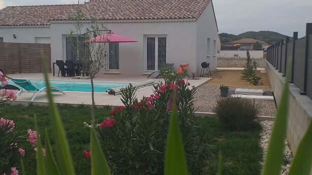 Une maison moderne avec une piscine, entourée d’un jardin agrémenté de fleurs roses et de plantes vertes.