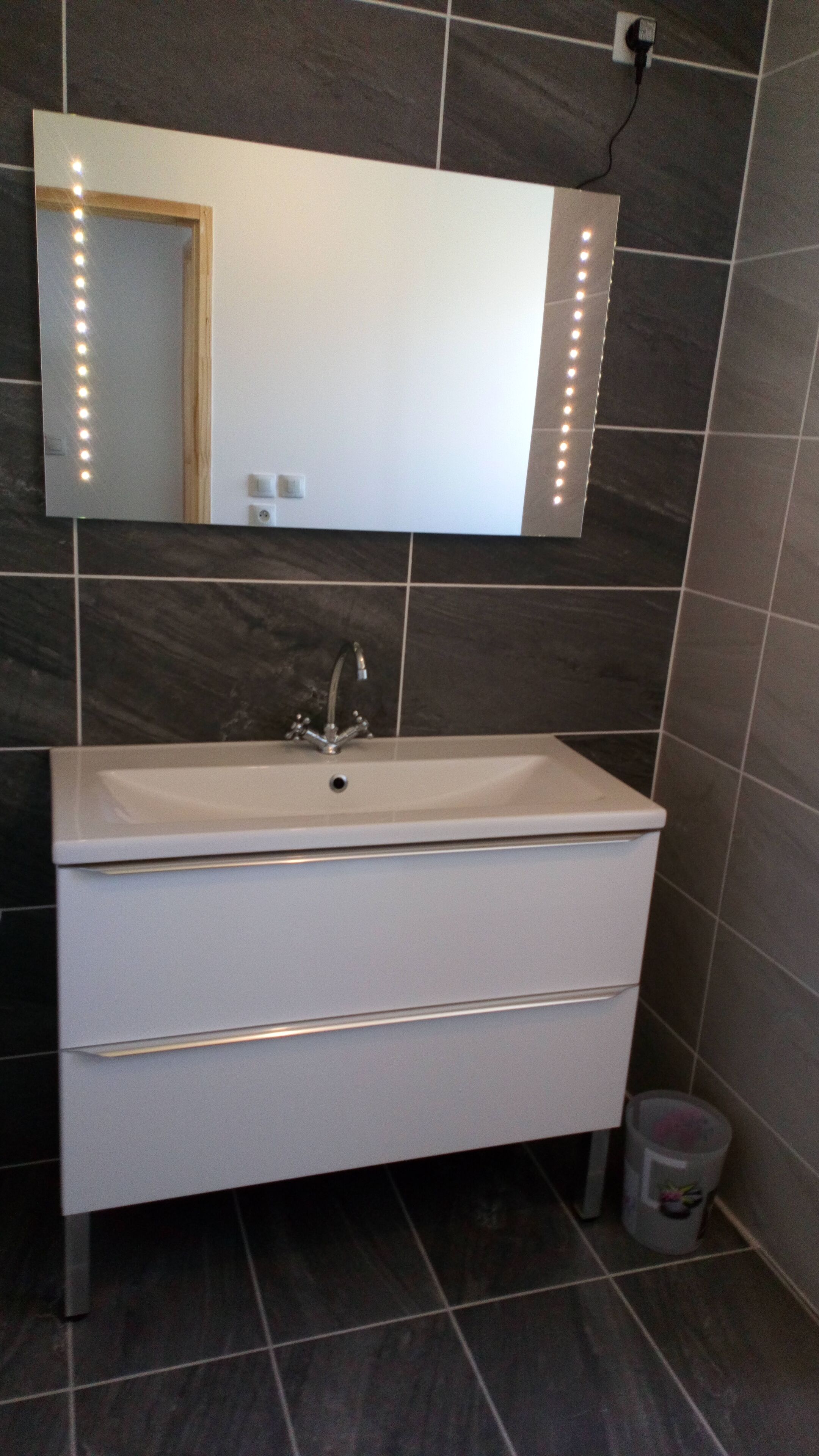Une salle de bain avec un lavabo blanc, un miroir et un luminaire fixé au mur.