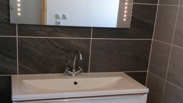 Une salle de bain avec un lavabo blanc, un miroir et un luminaire fixé au mur.