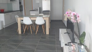 Une cuisine moderne avec des meubles blancs, un four à micro-ondes et un réfrigérateur. On y trouve également un coin repas avec une table en bois et des chaises blanches.
