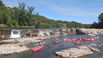 Kajakkers in roze kajaks bevaren een rivier met een waterval en rotsachtig terrein.