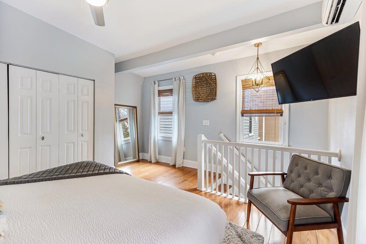 A bedroom with a large bed, a TV mounted on the wall, and a staircase leading to another room.