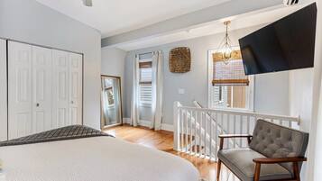 A bedroom with a large bed, a TV mounted on the wall, and a staircase leading to another room.