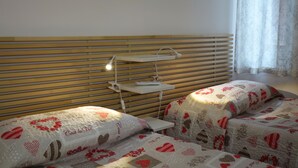 Et soveværelse med to senge, begge med dynebetræk med hjerter, et natbord med en lampe, og en sengegavl i træ.