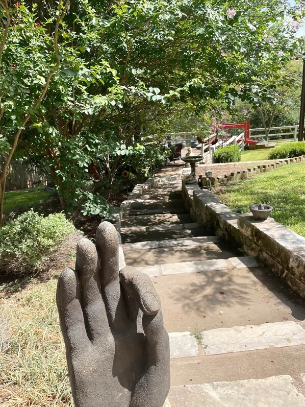 Un sendero de piedra que atraviesa un jardín, con una gran escultura de mano de piedra al frente.