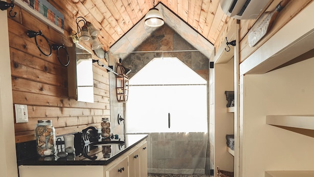 A rustic kitchen with wooden walls, a black countertop, and a view through a window to an outdoor area.