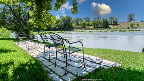 A riverside park with a picnic table and chairs under a tree.