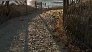 En sandstig som leder till havet, med ett trästaket på ena sidan.