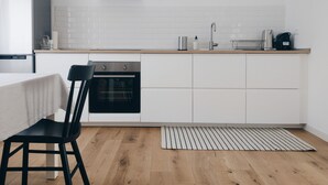 A modern kitchen with white cabinetry, a black oven, a stainless steel range hood, and a wooden floor.